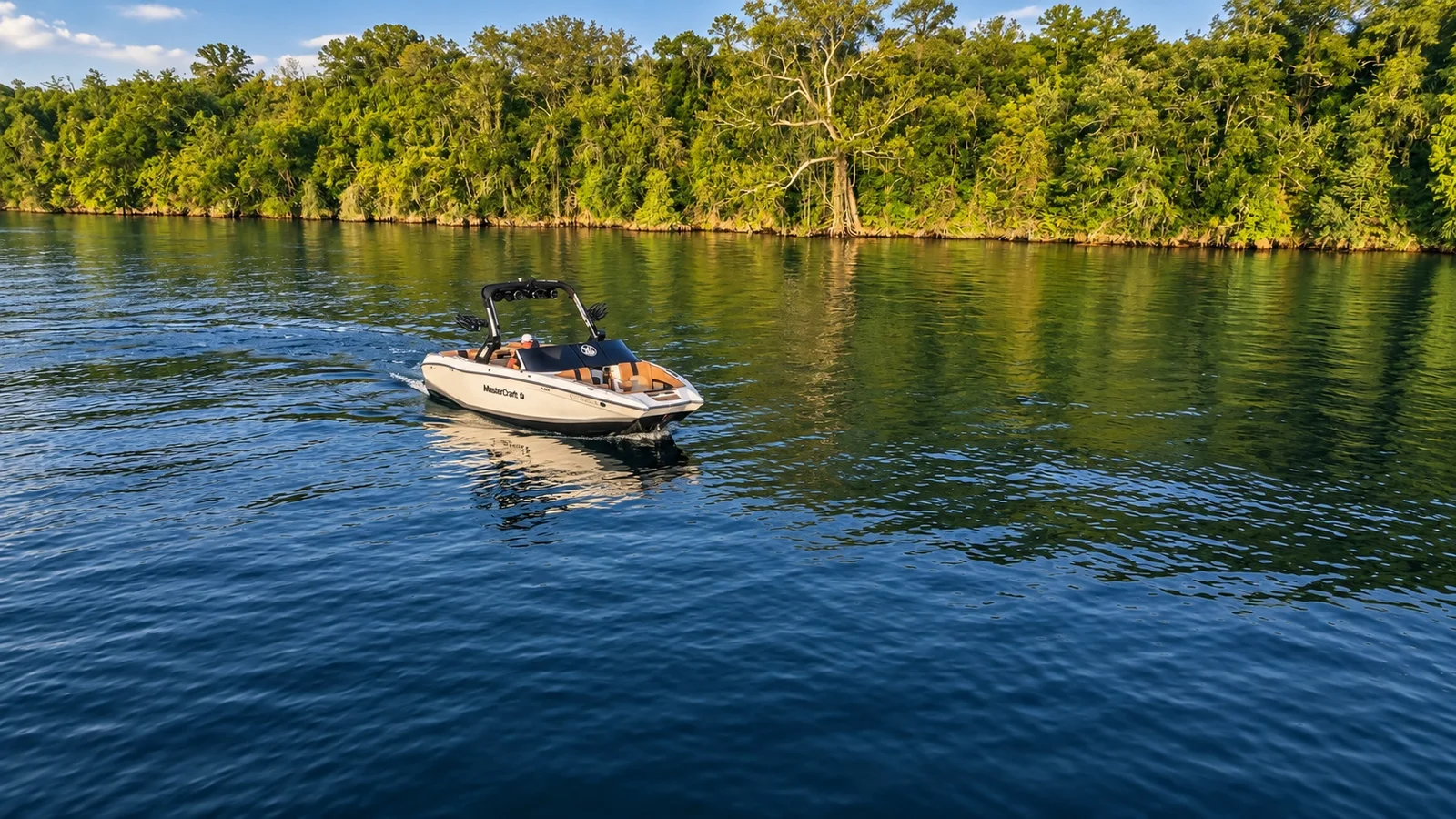 White MasterCraft cruising on the lake beside a wooded shoreline